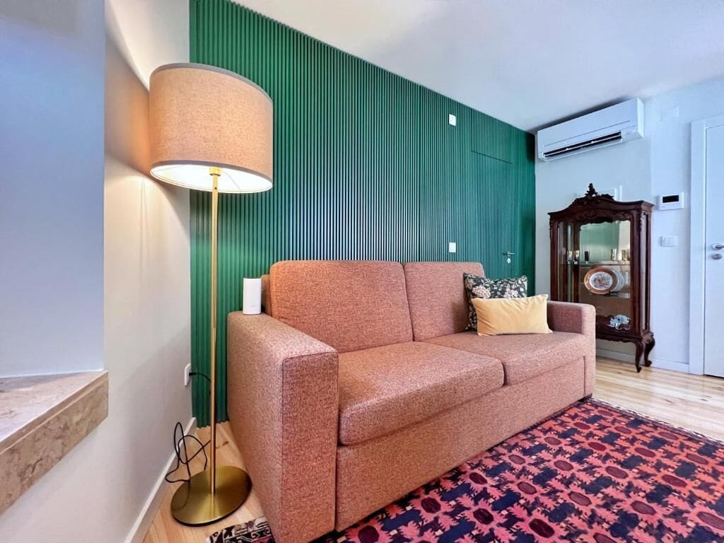 A living room with a sofa, a floor lamp, a patterned rug, a green wall, and a wooden cabinet.