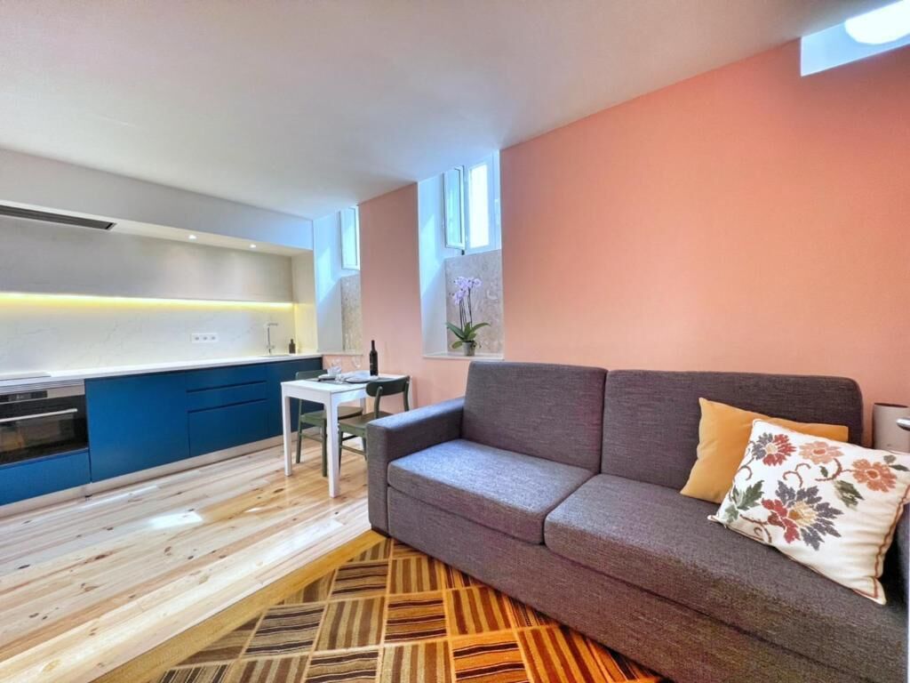 A modern living room with a sofa, a small table, and a kitchen area in the background.