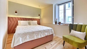 Un dormitorio con cama, ventana, una silla verde y suelo de madera.