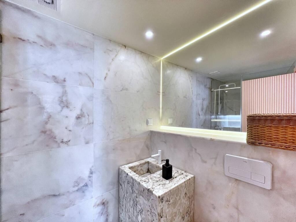 A bathroom with marble walls, a small sink, a mirror, and a light fixture.