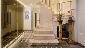 Una escalera con piso a cuadros que lleva a una plataforma, una pared con una obra de arte azul, y dos plantas en macetas sobre la plataforma.