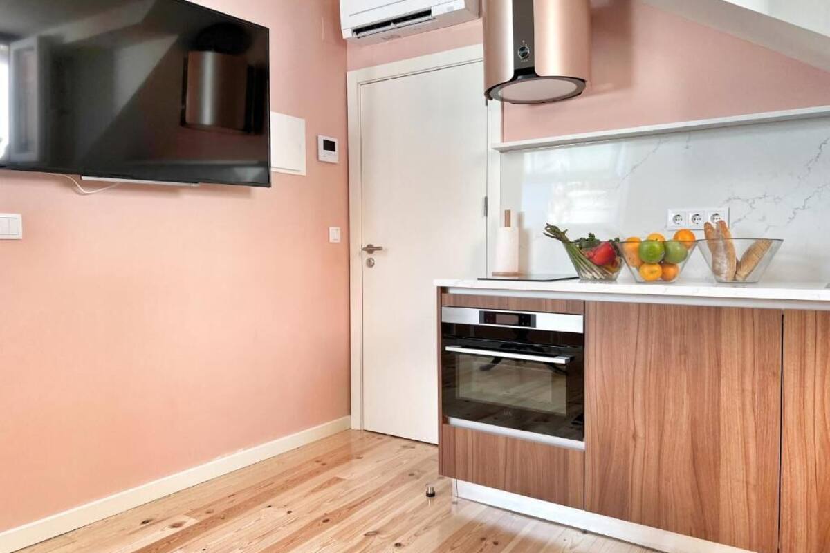 Una cocina compacta con horno empotrado, microondas y una pequeña encimera con frutas y pan.