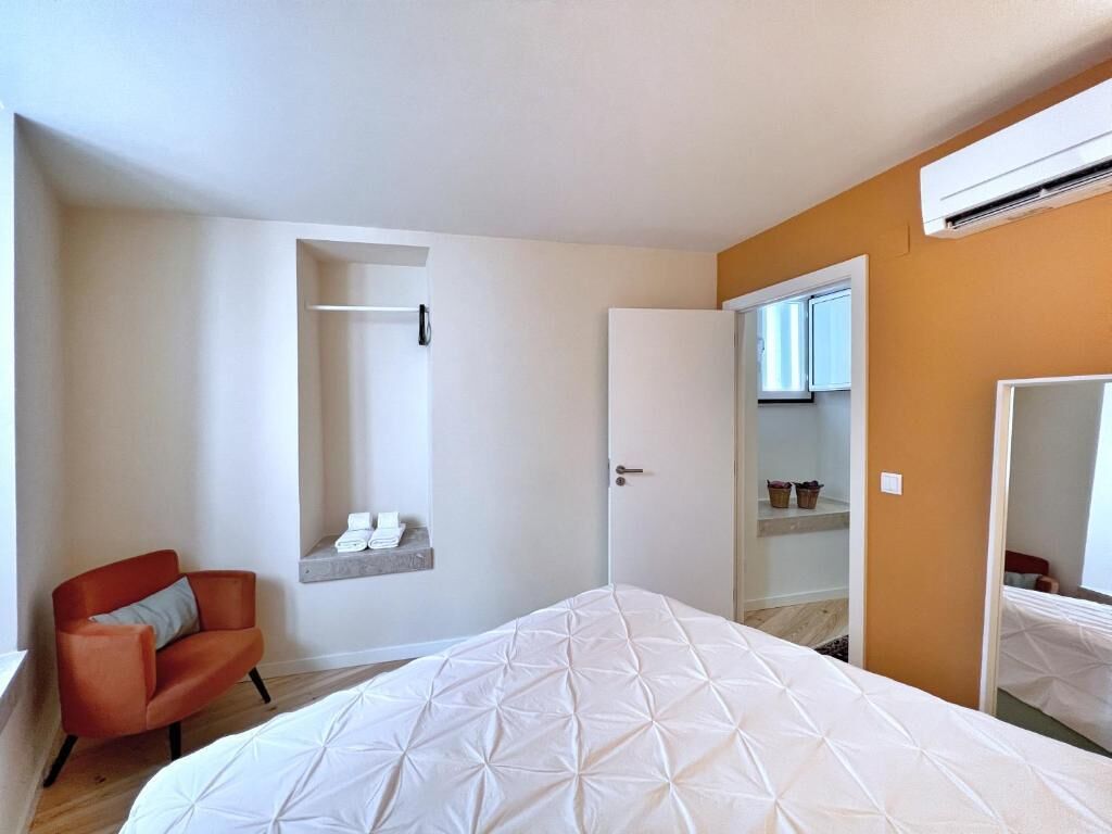 A bedroom with a bed, a chair, a wardrobe, and a small shelf with towels.