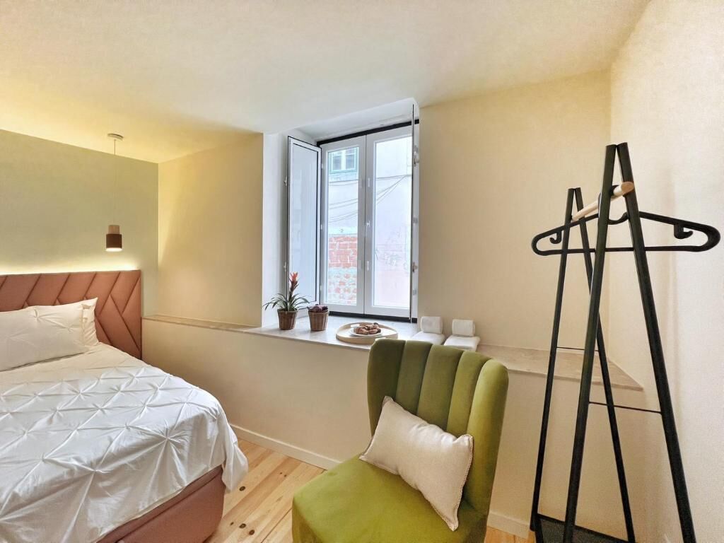 A bedroom with a bed, a window, a green chair, and a coat rack.