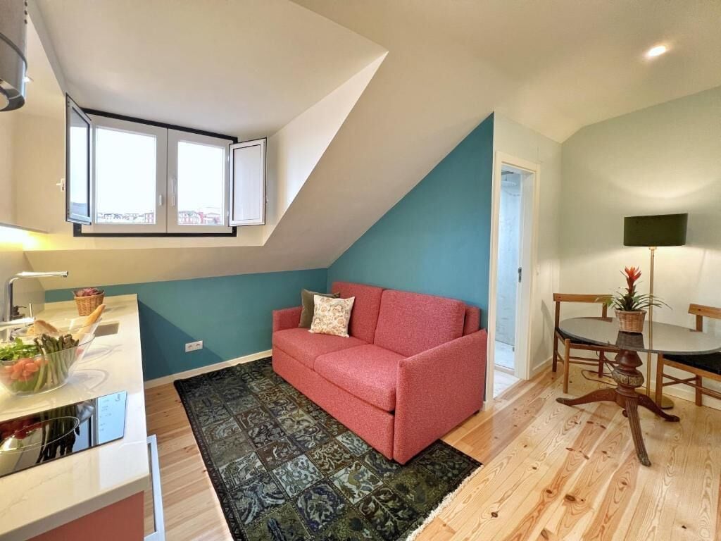 A compact living space with a kitchenette, a red sofa, a dining table, and a large window.