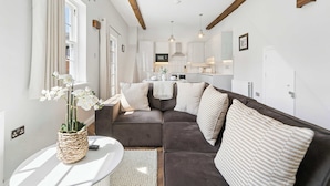 Een moderne woonkamer met een bank, een tafeltje met een vaas en een keuken op de achtergrond.