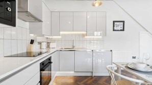 Een moderne keuken met witte kasten, een inbouwoven en een eethoek met een tafel en stoelen.