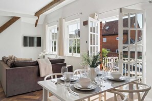 Ein modernes Wohnzimmer mit einer Couch, einem Esstisch für zwei Personen und einem großen Fenster mit Vorhängen.