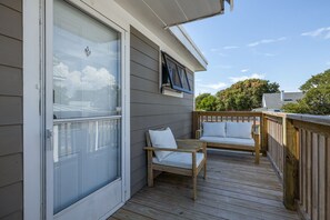 Eine Terrasse mit einer Schiebetür, einem Fenster mit Jalousien und zwei Holzstühlen mit Kissen.