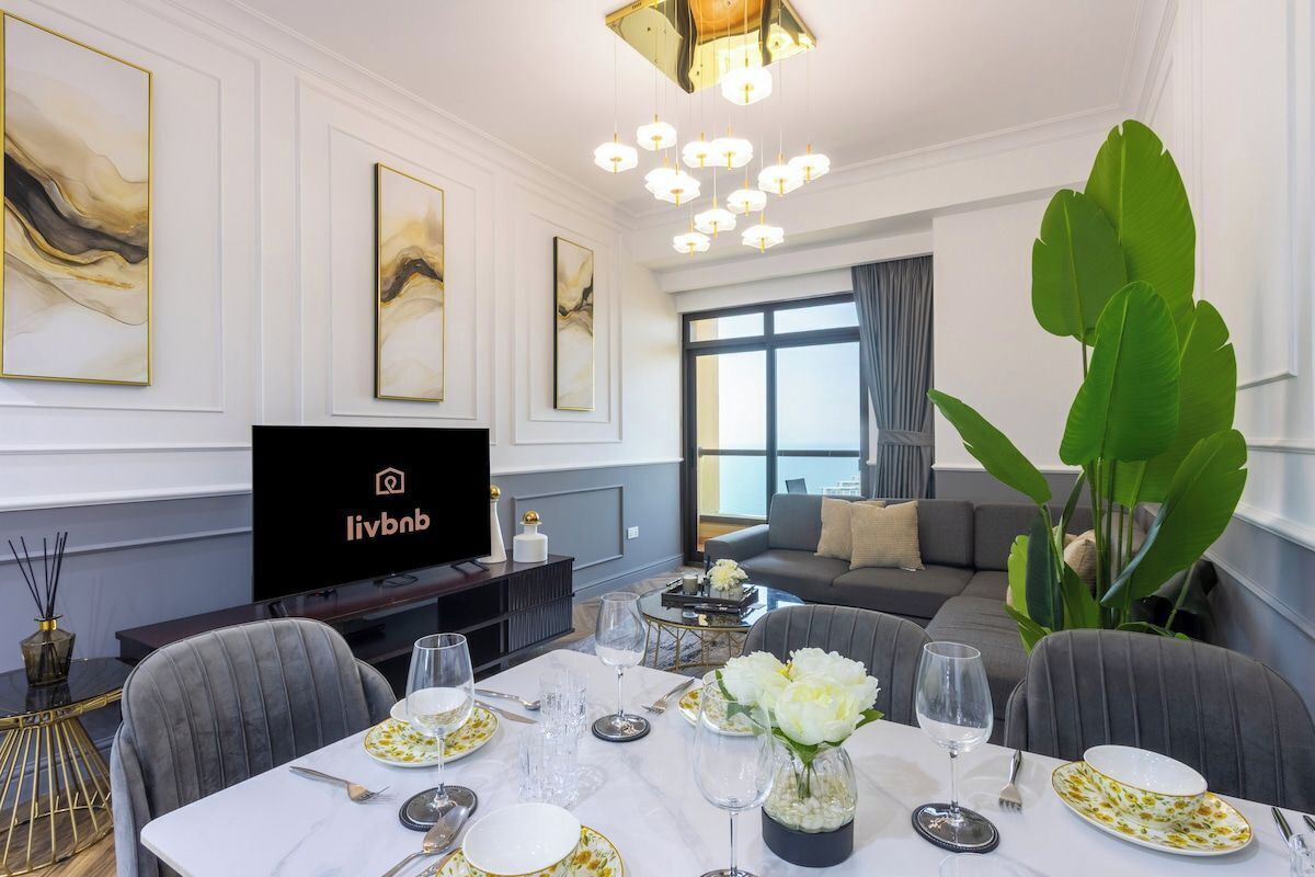 A modern living room with a dining area, a flat-screen TV, and a large plant.