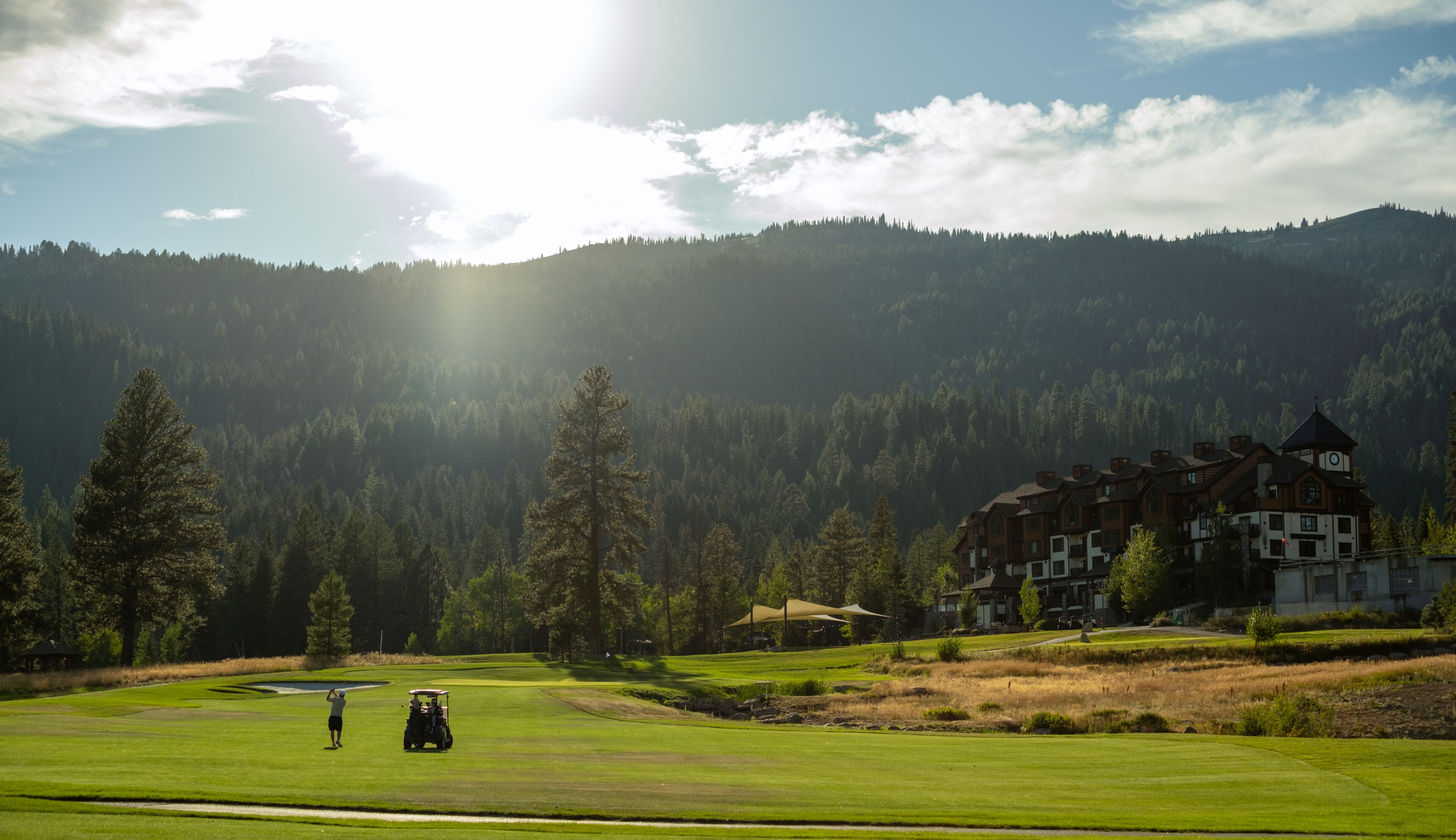 Un campo de golf con un club de campo, una persona jugando y un edificio grande con una torre de reloj al fondo.
