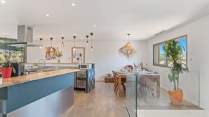 Een moderne keuken met een centraal eiland, een eetgedeelte met een glazen wand en een groot raam met uitzicht.