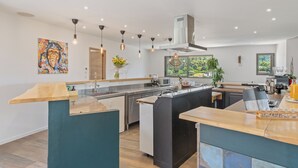 Een moderne keuken met een centraal eiland, hanglampen en een groot raam met uitzicht op groen.