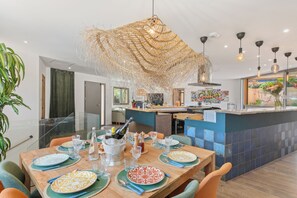 Uma área de jantar moderna com uma ilha central, um lustre e vista para a cozinha.