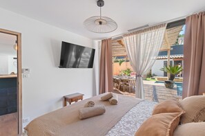 Quarto com cama, televisão, janela com cortinas e vista para área externa com piscina.