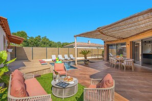 Um pátio com piscina, espreguiçadeiras, mesa de jantar e área de estar coberta.