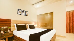 A hotel room with a large bed, a wooden headboard, a nightstand with a phone, a small table, and framed artwork on the wall. - Saver Double Hotel O Chandigarh Road (Dera Bassi)