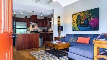 A modern kitchen with a central island, a dining area with a sofa and table, and a living room with a couch and a painting on the wall.