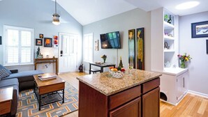 Eine moderne Küche mit Granit Arbeitsplatten, ein Essbereich mit einer Couch und einem Couchtisch, und ein Wohnzimmer mit Fernseher und Kunstwerken.