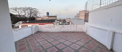 A rooftop terrace with a patterned floor, a satellite dish, and a view of surrounding buildings.