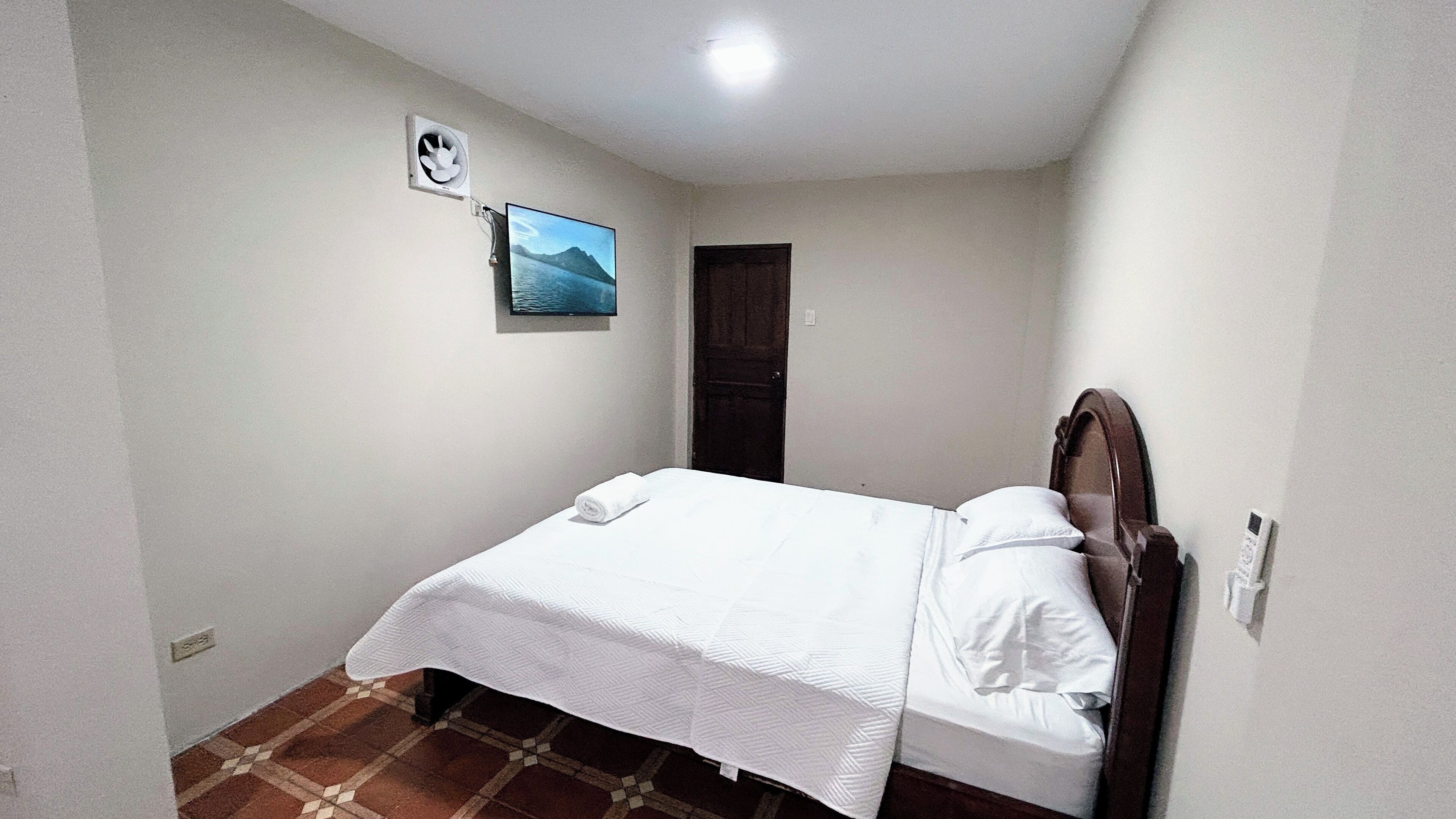 A small, clean room with a single bed, a wall-mounted air conditioner, and a door.