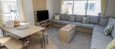 Uma sala de estar moderna com sofá, televisão, mesa de centro de madeira e uma mesa de jantar com cadeiras.