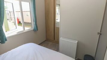 A bedroom with a bed, a window with curtains, a radiator, and a door leading to a hallway.