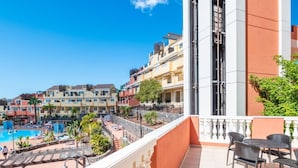 Un balcon avec vue sur la piscine, un espace salon extérieur et un ciel dégagé.