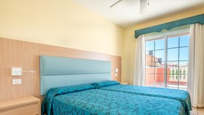 Une chambre d’hôtel avec deux lits, une tête de lit en bois, une petite table de chevet et une fenêtre avec des rideaux.