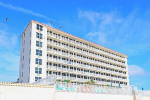 A multi-story hotel with balconies, a red roof, and a clear blue sky. - HBR 507 luxury beach view condo with pool, hot tub and more. (Daytona Beach)