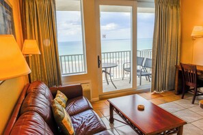 A room with a leather sofa, a wooden table, a balcony with a view of the ocean, and a chair. - HBR 507 luxury beach view condo with pool, hot tub and more. (Daytona Beach)