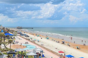 A beach with a pool, umbrellas, and a pier in the background. - HBR 507 luxury beach view condo with pool, hot tub and more. (Daytona Beach)