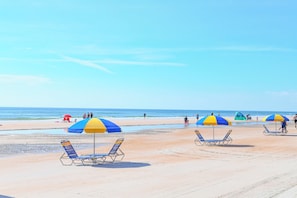 A beach with sun loungers and umbrellas, a clear sky, and the ocean in the background. - HBR 213 Flamingo Oasis with pool and hot tub. (Daytona Beach)