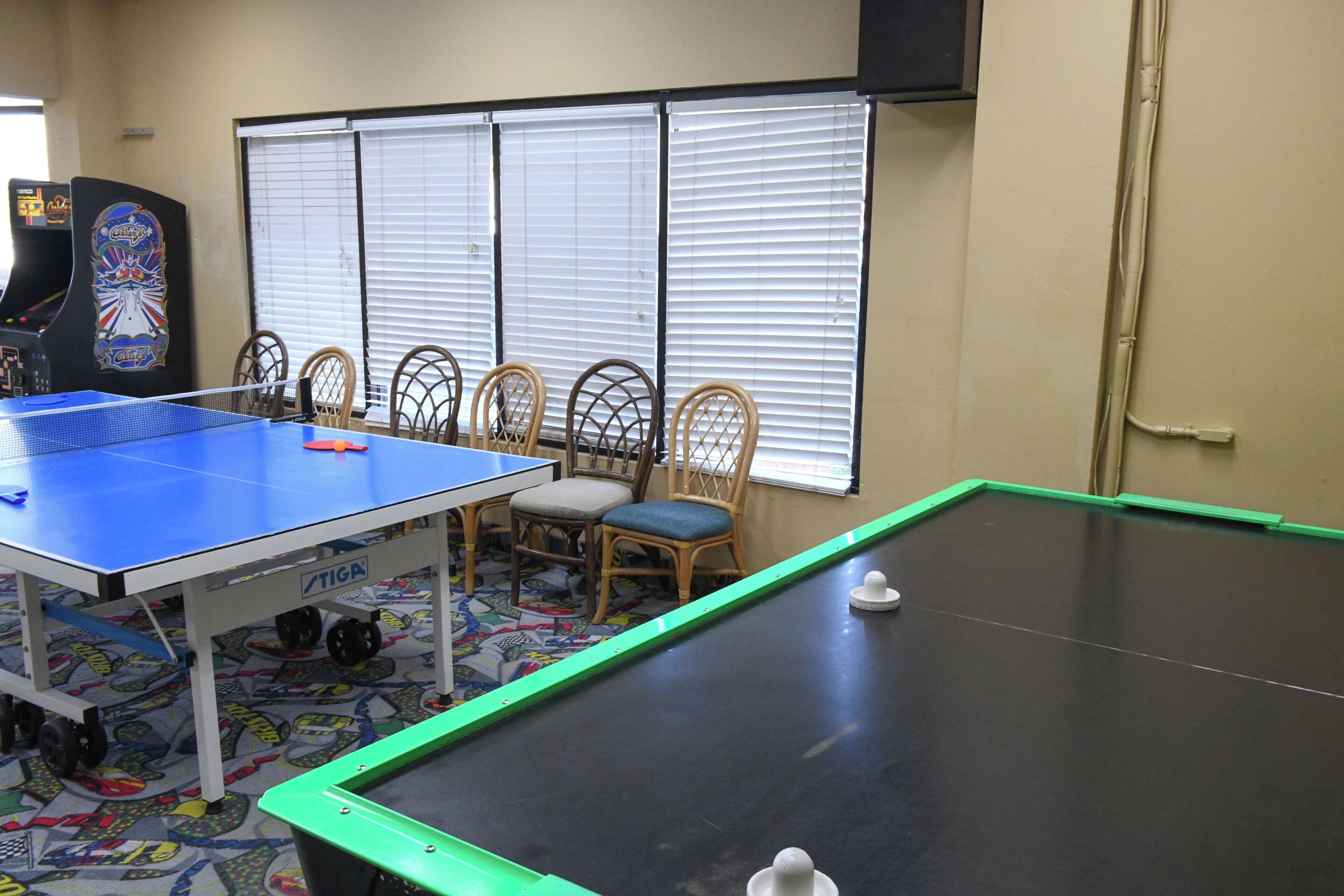 Une table de ping-pong, des chaises et une petite table de billard dans une pièce dotée de fenêtres et de jeux d’arcade.