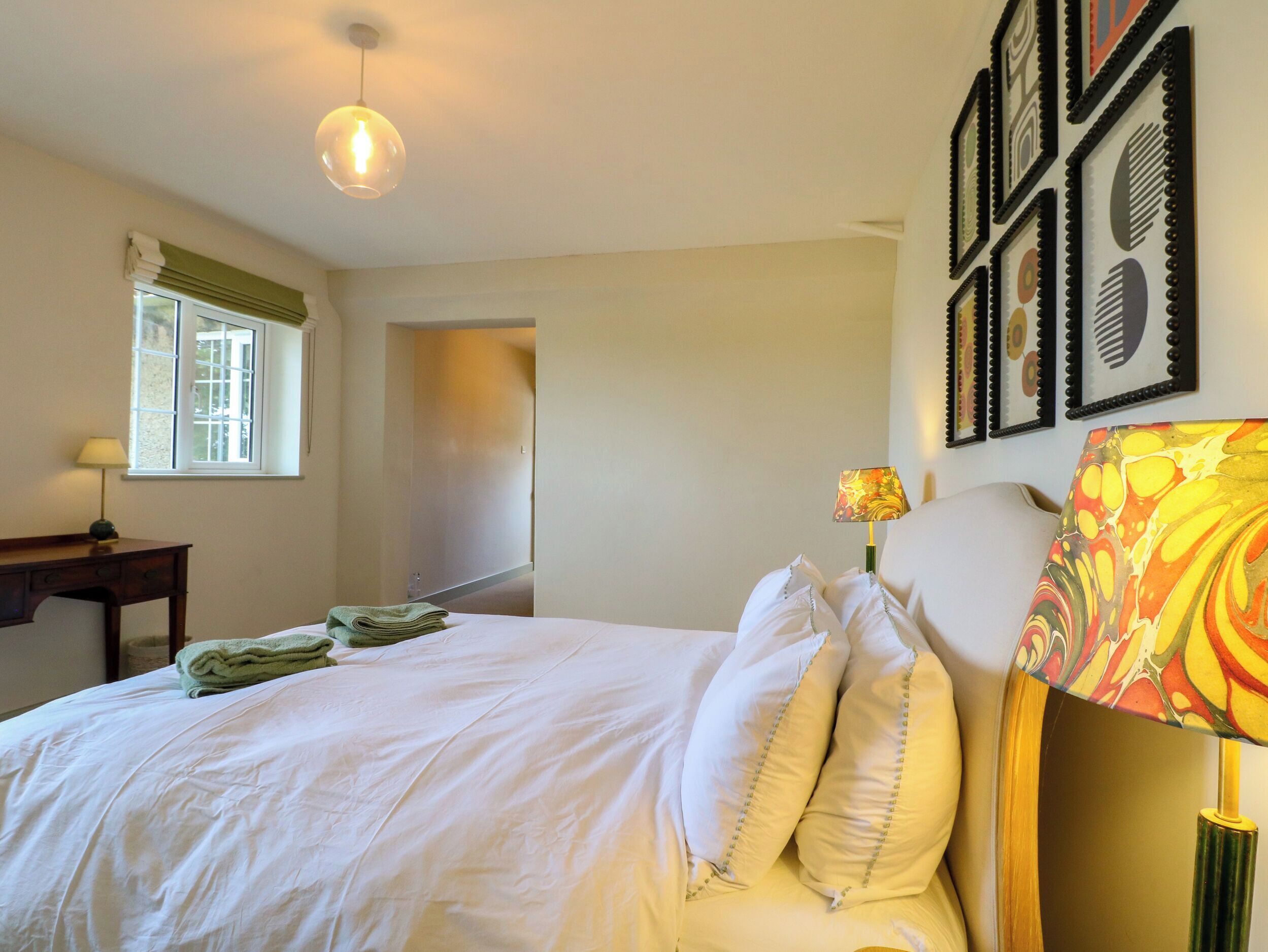 A bedroom with a bed, a desk, a window, and a wall with framed artwork.