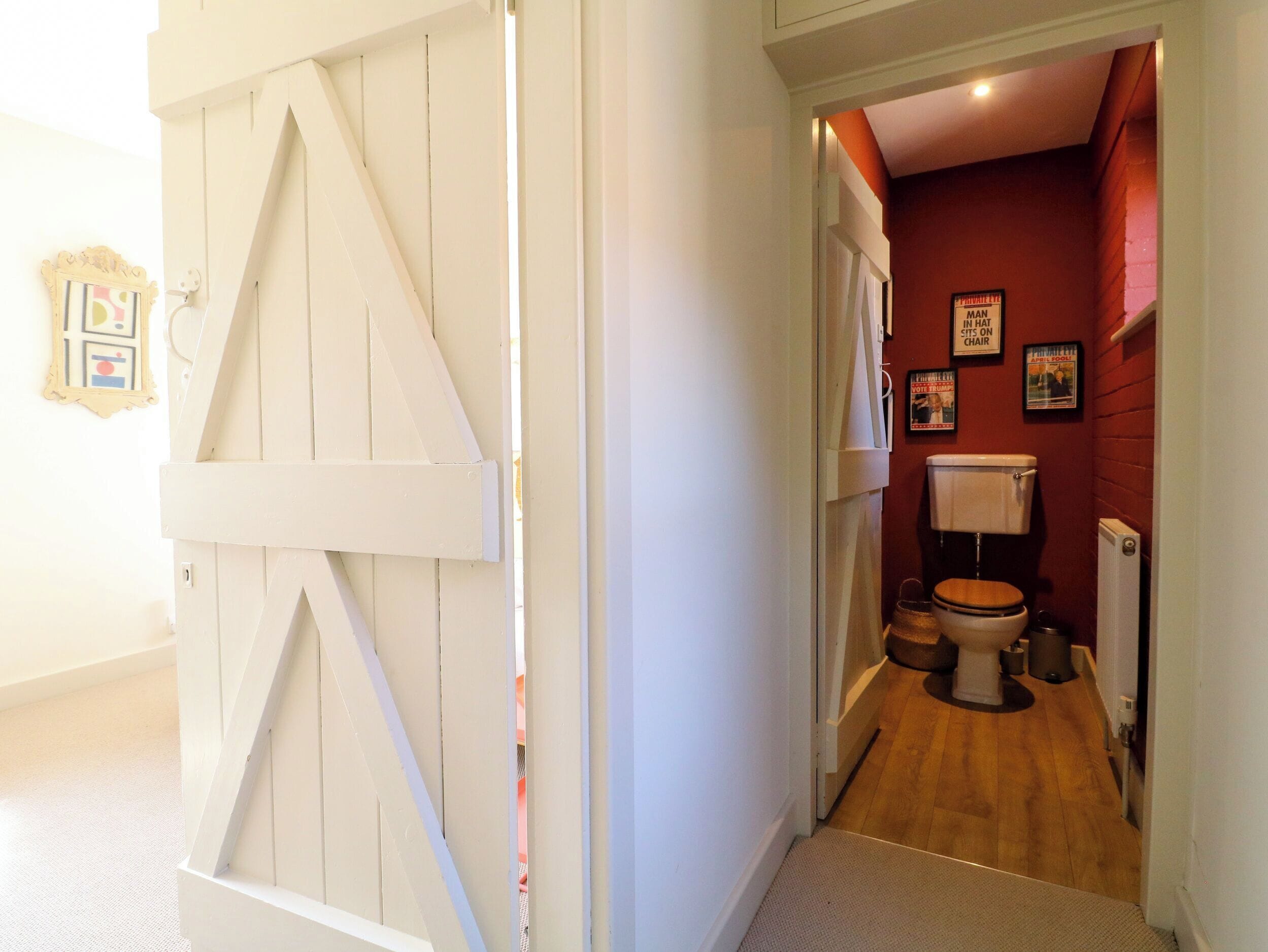 Un couloir étroit mène à une salle de bain équipée de toilettes, d’un radiateur et dotée d’un plancher en bois.