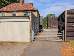 A gated driveway leading to a building with a tiled roof and a garage. - The Stable Flat (Melton Mowbray)