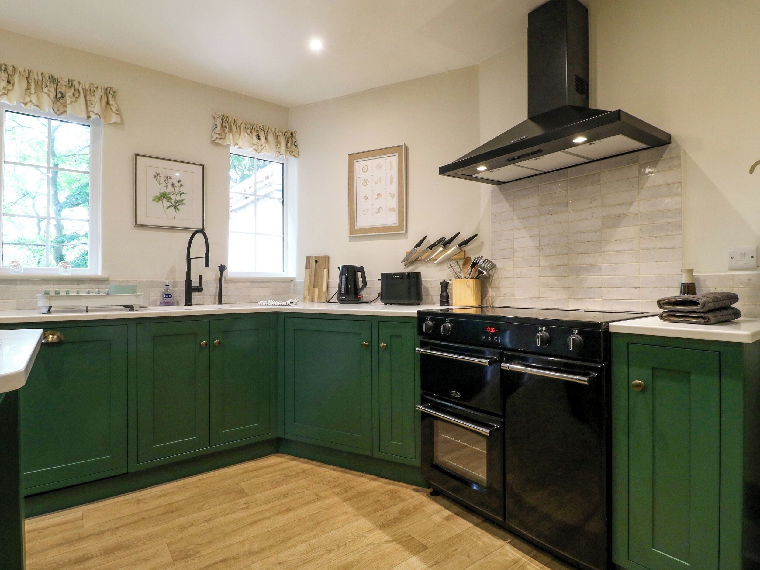 A kitchen with green cabinets, a black stove, and a window with a view of trees.