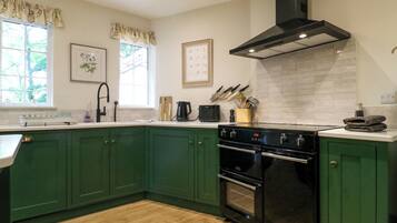 A kitchen with green cabinets, a black stove, and a window with a view of trees.