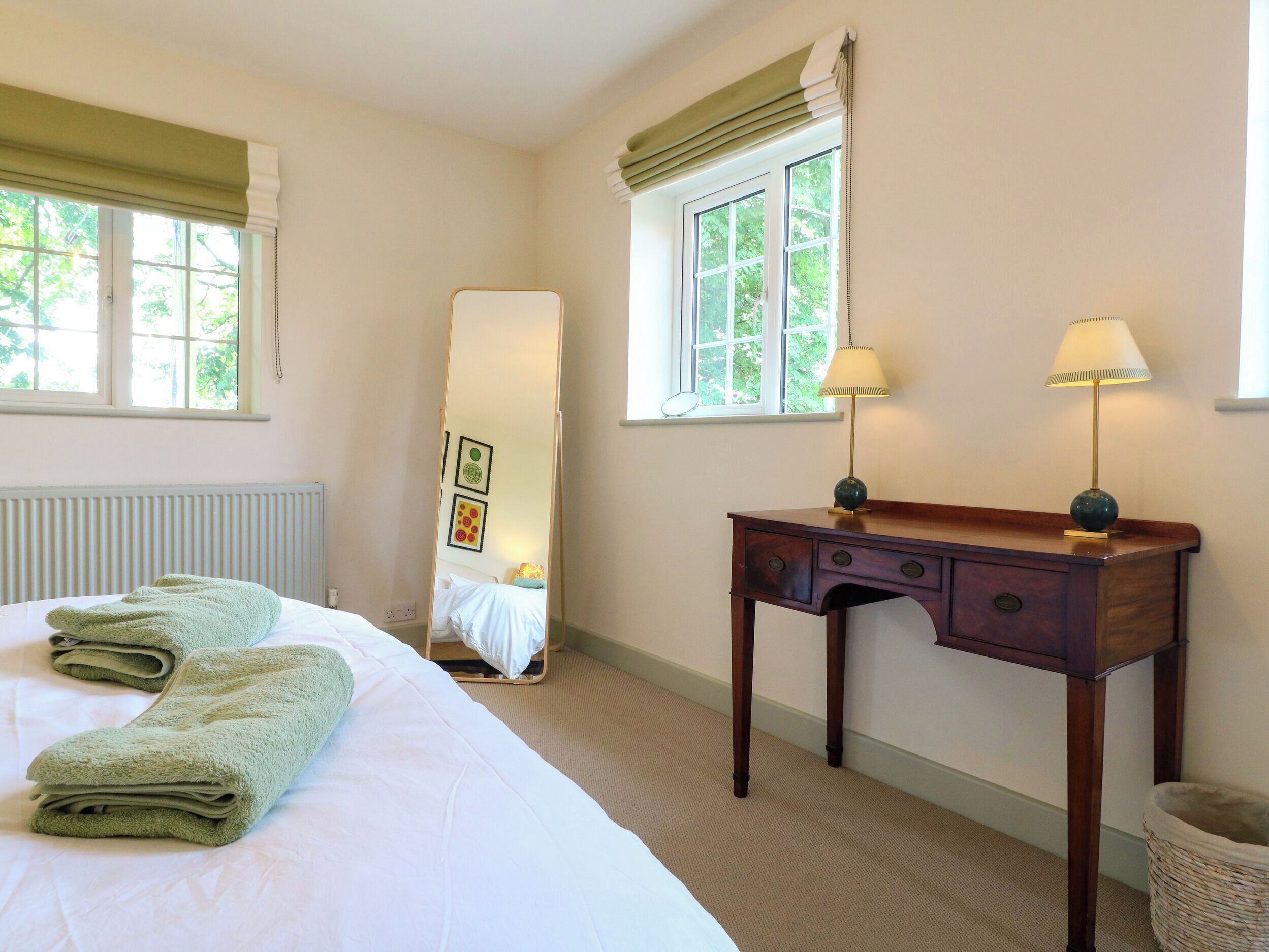 Habitación de hotel con cama, dos lámparas de noche, un espejo grande y una ventana con cortinas.