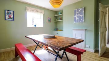A dining area with a wooden table, benches, a hanging light fixture, a window with blinds, and a fireplace.