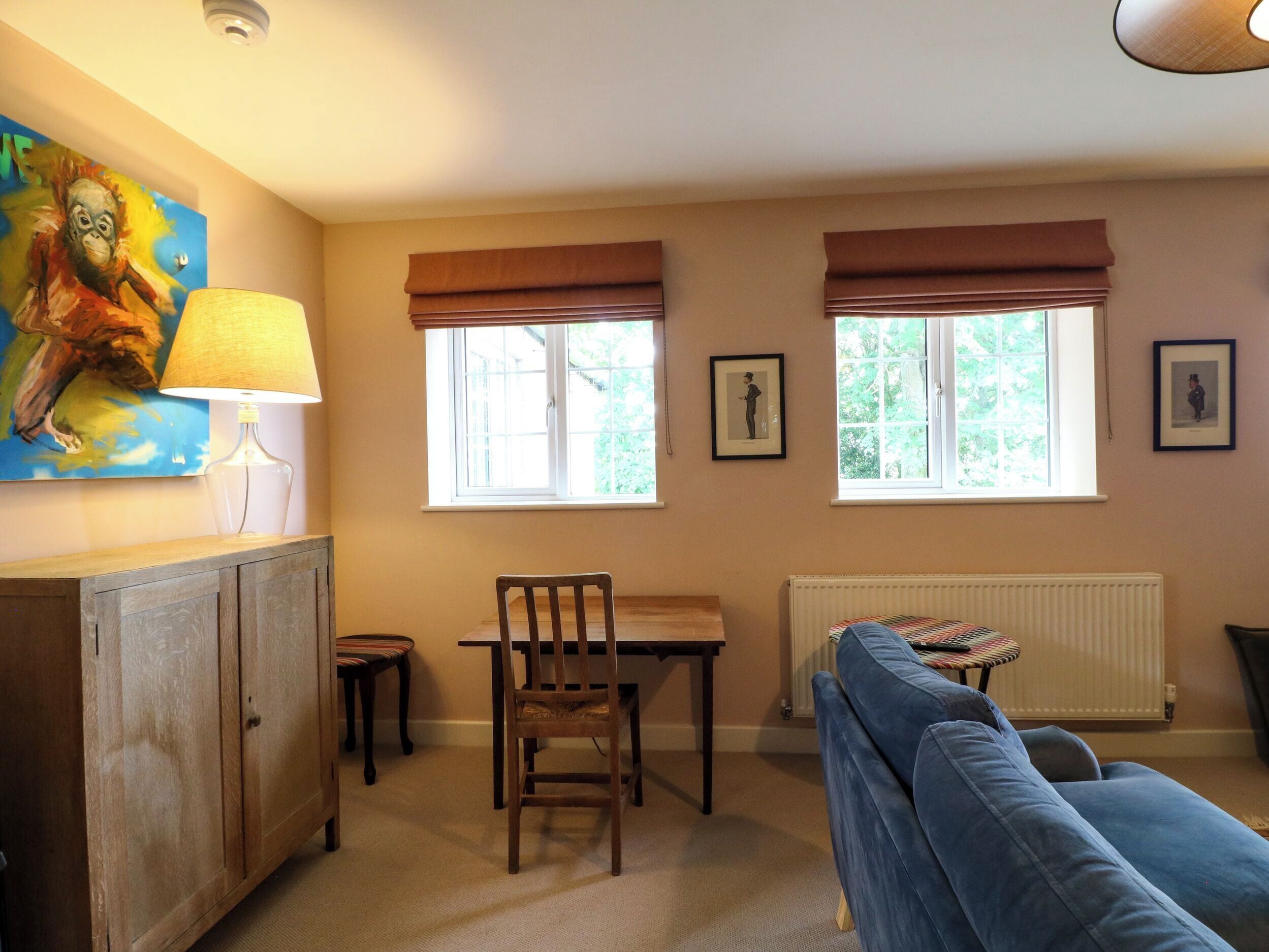 Une pièce comprenant une table à manger, des chaises, un canapé, un radiateur et deux fenêtres équipées de stores.