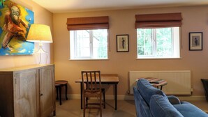 Una habitació amb taula de menjador, cadires, un sofà, un radiador i dues finestres amb persianes.