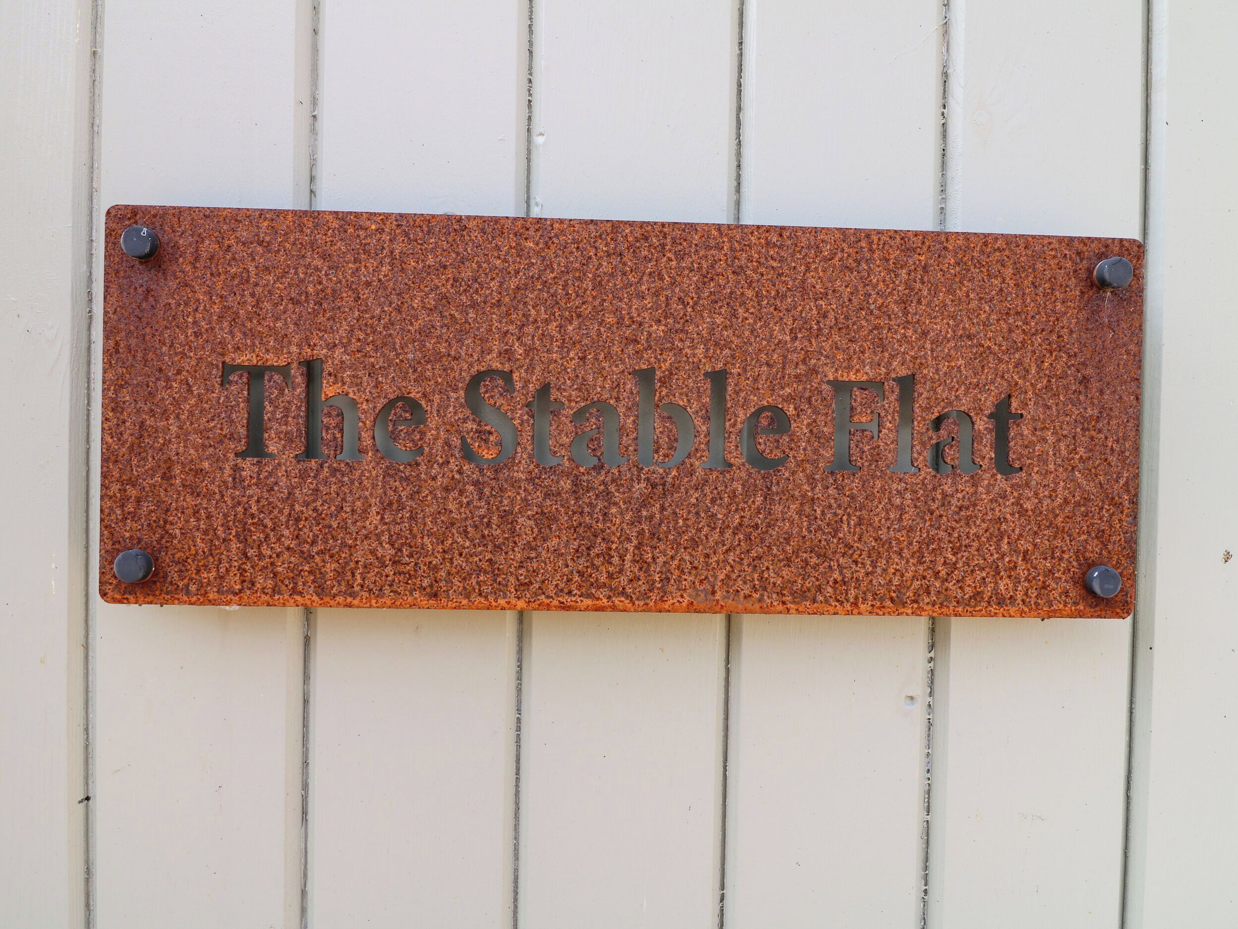 Una placa de metal con la inscripción 'The Stable Flat' colocada sobre una pared blanca.