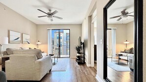 Amplia sala de estar con un ventanal grande, ventiladores de techo y vistas a un edificio.
