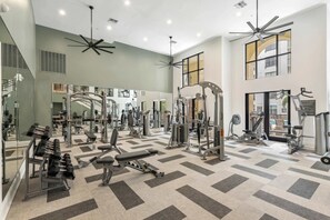 Ein geräumiger Fitnessraum mit verschiedenen Trainingsgeräten, großen Spiegeln und einem gemusterten Boden.