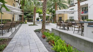 Un patio al aire libre con mesas, sillas, palmeras y un sendero.