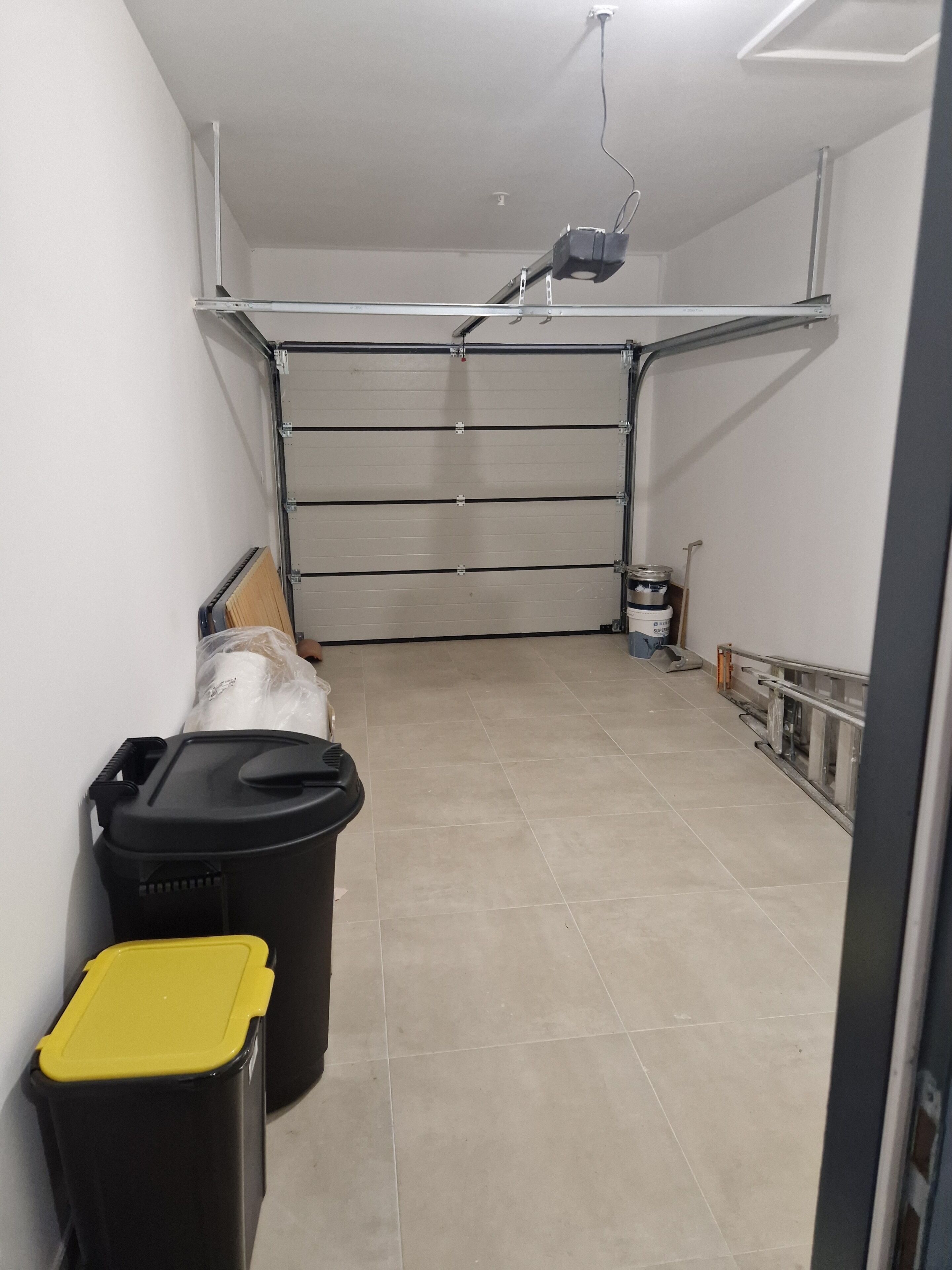 Un garaje con una puerta cerrada, un proyector en el techo y dos botes de basura.