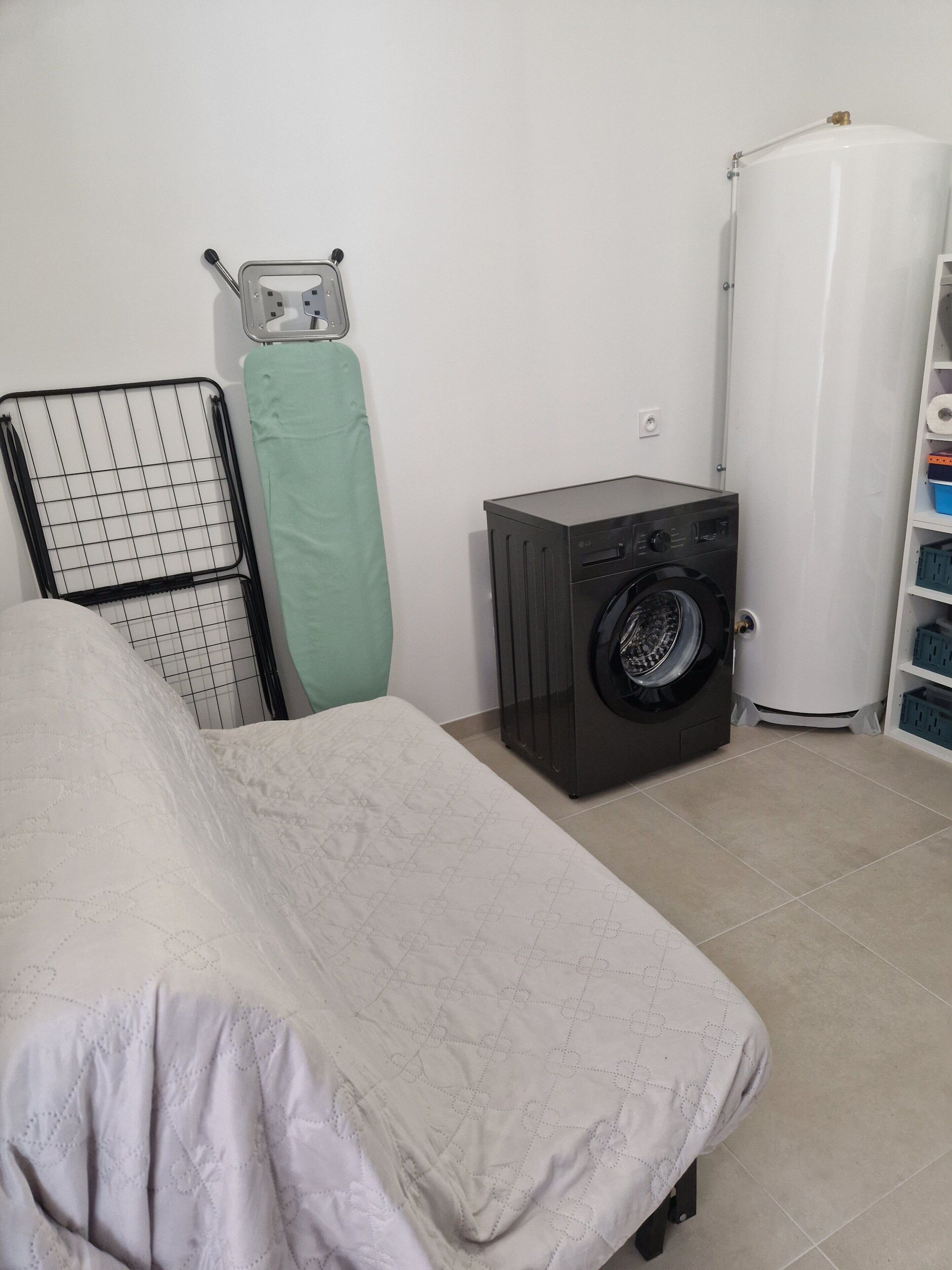 Een slaapkamer met een bed, een wasmachine, een radiator en een boiler.