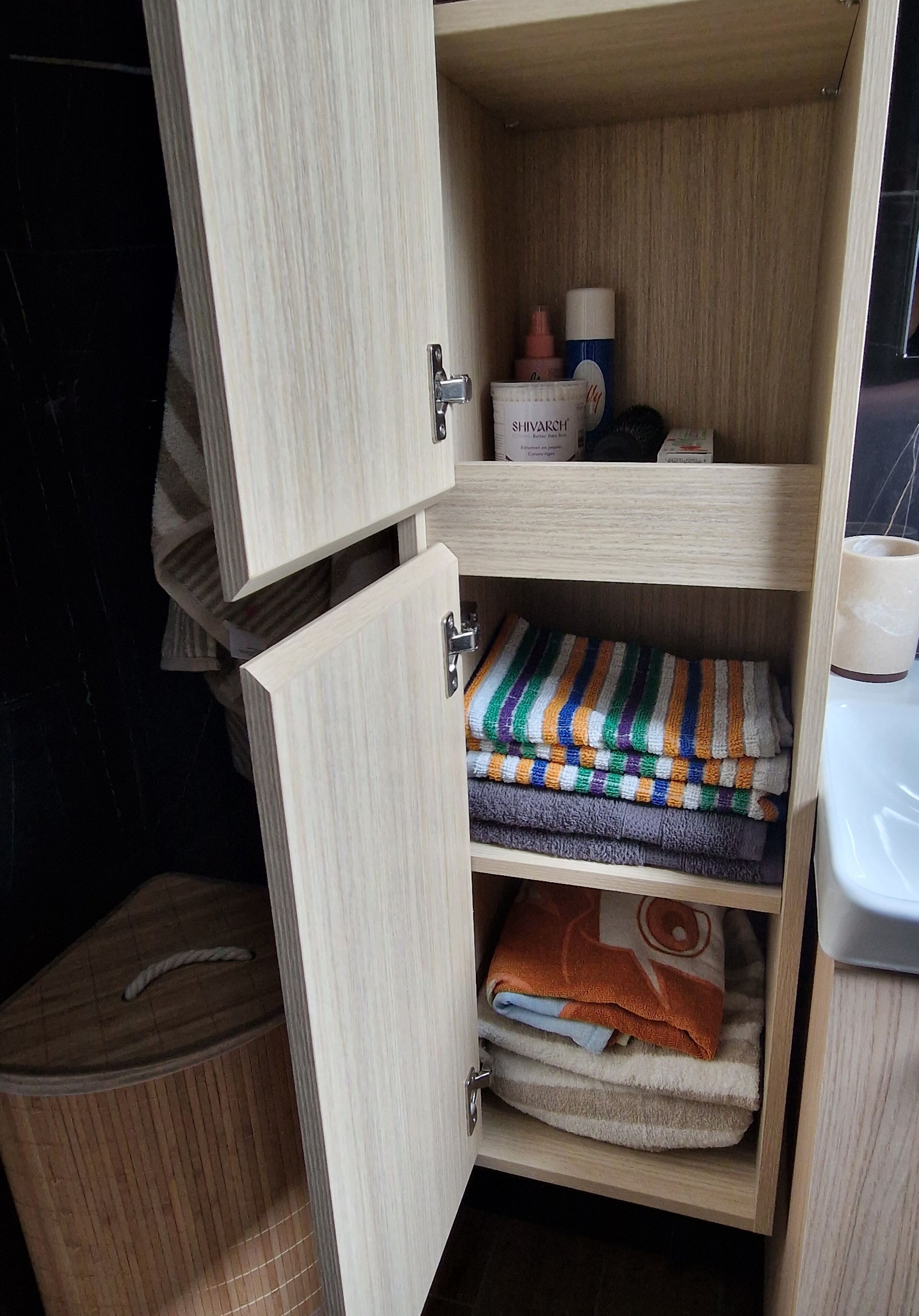 A wooden cabinet with a drawer containing folded towels and a container labeled 'SHIVARCH.'